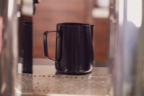 Classic matt surface stainless steel milk frothing pitcher mug with handle sit on table.  Kitchen tool, heat-resistant and durable.