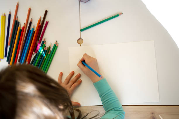 The girl photographed from the back and from the top point drawing with a pencil on a white backgroundThe girl with pigtails photographed from the back and from the top point drawing with a colorful pencil on a white background