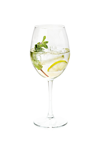Refreshing Cocktail with Basil Leaf, Lime and ice in a wine glass on a dark background. drink gin and tonic