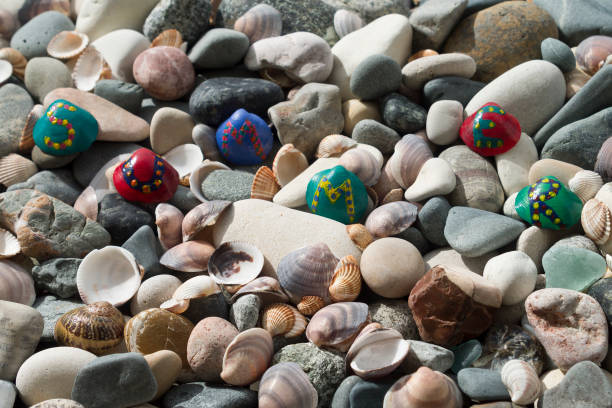 Beach stones and seashell background with bright painted seashells with letters forming word Summer in sunlight