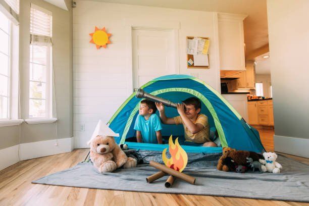 Boys Exploring with Telescope Indoors Two brothers camp inside their home due to the coronavirus restrictions and quarantine. They have pitched a tent along with their stuffed animal friends and have a fake campfire next to their tent. They are searching the skies for stars and dreams. staycation photos stock pictures, royalty-free photos & images