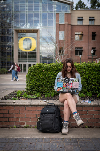 Eugene, Oregon - January 31, 2020: A student sits outdoors working on her laptop on the University of Oregon campus. The university was founded in 1876 and recently had an enrollment of nearly 20,000 undergraduate students.