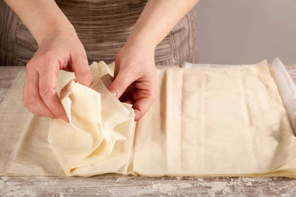 mujer que separa hojas de pasta de filo para cocinar una receta saludable - pastry crust fotografías e imágenes de stock