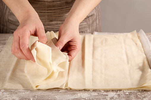 Woman separating phyllo pasta leaves to cook a healthy recipe. Concept of healthy home cooking.