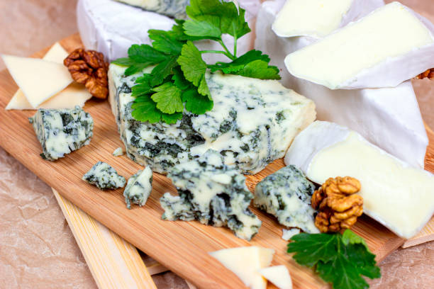 many different varieties of cheese: blue, brie, camembert and other with walnuts on wooden board background - cheese emmental cheese swiss culture cutting board imagens e fotografias de stock