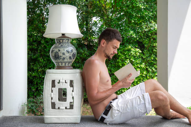 um jovem lê um livro no terraço de verão - balcony beach book men - fotografias e filmes do acervo
