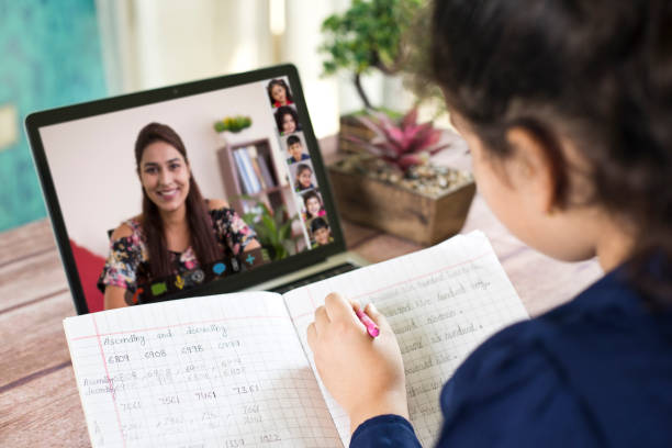 Distance learning from home on video conference call Girl participating in online education training class with teacher and other students using laptop at home over the shoulder view photos stock pictures, royalty-free photos & images