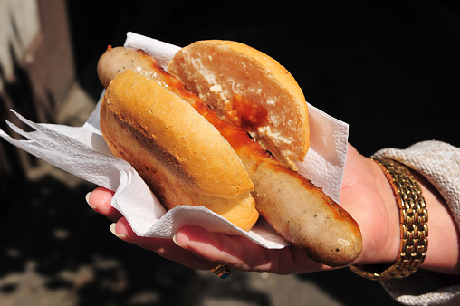 A grilled bratwurst served inside a bread bun and held in a ladies hand