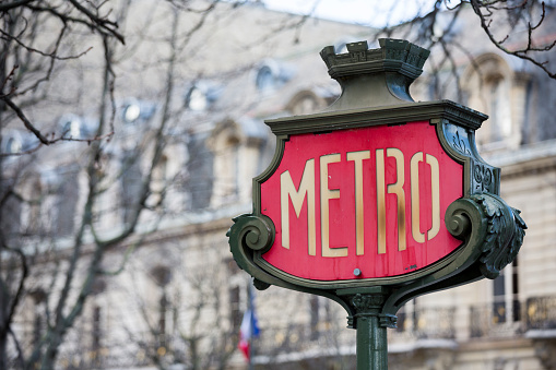 The Paris Metro sign on an old, ornate wrought iron stand, indicating the presence of the subway system entrance.