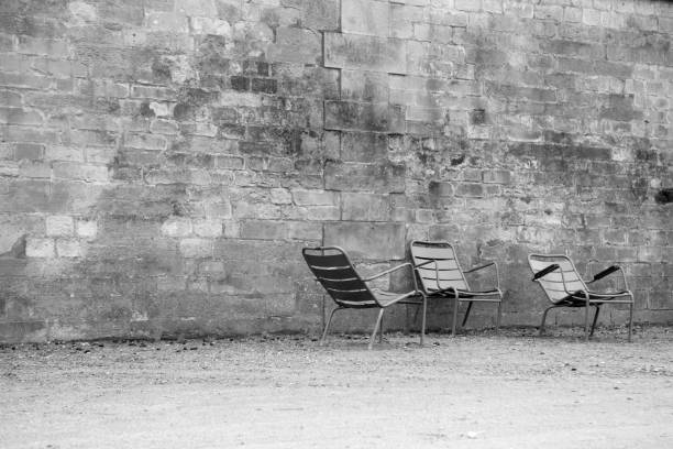 Three empty chairs against an old, worn brick stone wall in the Tuileries Garden in Paris, France in winter, conveying solitude or loneliness.