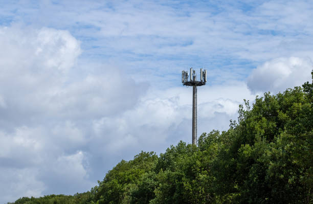 antena de telecomunicação atrás de árvores, céu azul nublado - mastro - fotografias e filmes do acervo