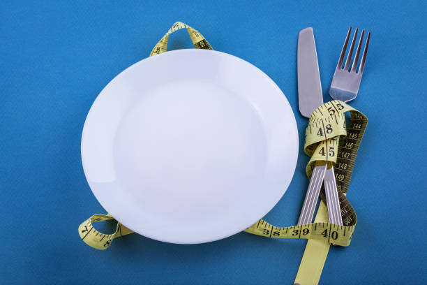 istock Empty white plate with devices on a blue background with yellow measuring tape tied. Weight loss concept. Cutlery close-up. 1226809606