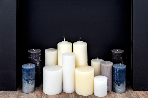 Multi-colored round cylindrical candles in a black fake fireplace.