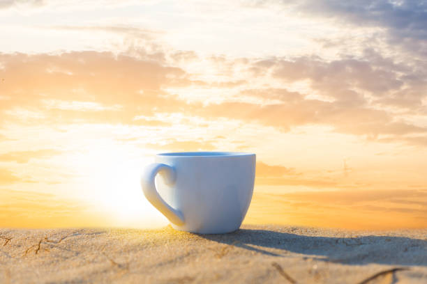 nahaufnahme kaffeetasse aufenthalt auf einem sand bei sonnenuntergang, outdoor-kaffee hintergrund - friable stock-fotos und bilder