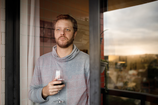 Man drinking wine on balcony behind glass window.