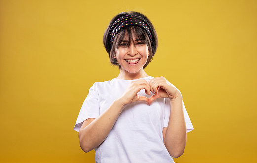 beautiful woman making heart shape with her hand front of yellow background.