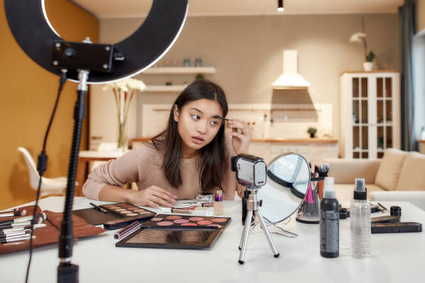 istock Look beautiful. Asian female blogger testing cosmetic products and makeup brushes while recording a tutorial video for her beauty blog using camera at home 1226816855
