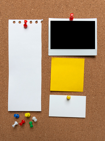 Bulletin board with yellow adhesive note, instant print photo, papers and thumbtacks.