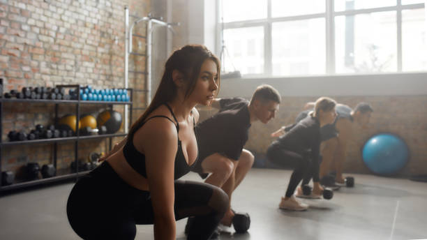 istock Fitness Journey. Young focused woman exercising with dumbbell while having workout at industrial gym. Group training concept 1226817271