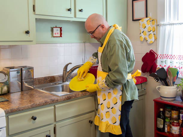 istock Man in frilly yellow apron washing dishes 1226818460