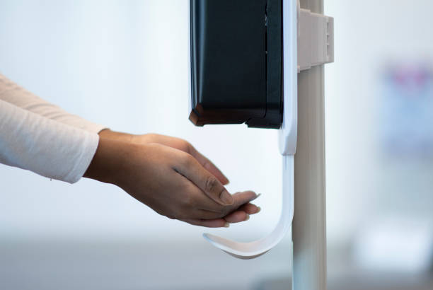 Medical Professional using a touchless sanitizer dispenser Female medical professional putting their hands under an automatic sanitizer dispenser at the hospital to ensure their hands are clean and germ free. soap dispenser stock pictures, royalty-free photos & images