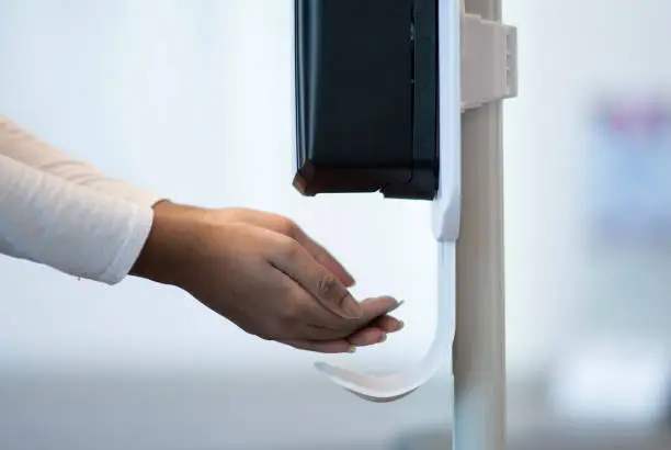 Female medical professional putting their hands under an automatic sanitizer dispenser at the hospital to ensure their hands are clean and germ free.