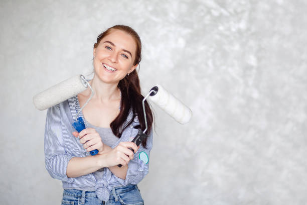 una ragazza bruna sta riposando mentre ripara una casa. una giovane bella donna sorridente in abiti casual tiene un rullo di vernice per un dipinto murale isolato su uno sfondo grigio. - painting home improvement decorating cut out foto e immagini stock