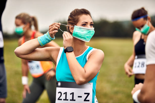 młoda sportsmenka zakłada ochronną maskę na twarz podczas przygotowań do maratonu. - jogging running motivation group of people zdjęcia i obrazy z banku zdjęć