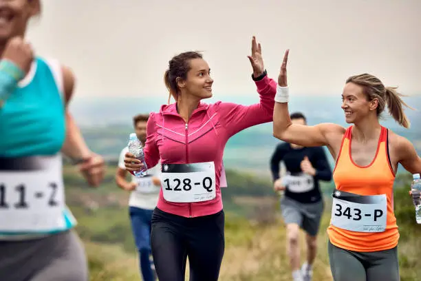 Happy marathon runners giving high-five to each other during the race in nature.