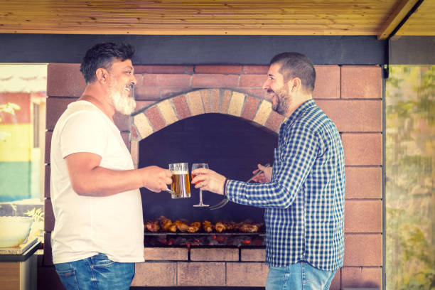 multiracial männliche freunde spaß beim kochen von fleisch auf grill, während alkohol trinken - barbecue chicken fotos stock-fotos und bilder