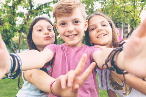 Happy best friends kids taking selfie outdoors at backyard party Best friends taking selfie outdoors in backyard – happy friendship with smart kids having fun celebrating summer vacation – modern children enjoying time together at garden party playing and smiling pre adolescent child stock pictures, royalty-free photos & images