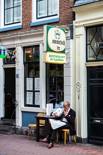 Amsterdam, Netherlands - September 8, 2018: Senior man smoking and reading a newspaper on the terrace of a bar in the old town of Amsterdam, Netherlands