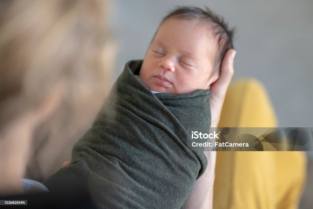 Caucasian mother holding her swaddled newborn Young mother holding her newborn baby while gently rocking in a rocking chair. Baby Blanket Stock Photo