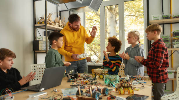 istock Working process. Young creative male teacher explains for students the principle of robotic machines work while holding console controller. Science and education. 1226826303