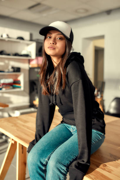 istock Any design you want. Cheerful female worker looking at camera while posing in custom apparel, baseball cap and hoodie. Young woman working at custom T-shirt, clothing printing company 1226826389