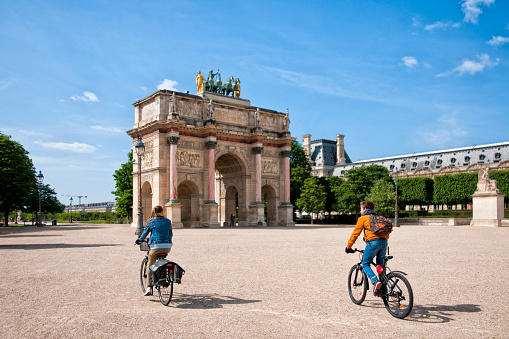 Paris : Arc de Triomphe du Carroussel, near Louvre with a couple of cyclists. The Louvre museum is closed, the place is empty, without tourists, few days after the Covid19 virus lockdown. Paris in France. May 11, 2020.