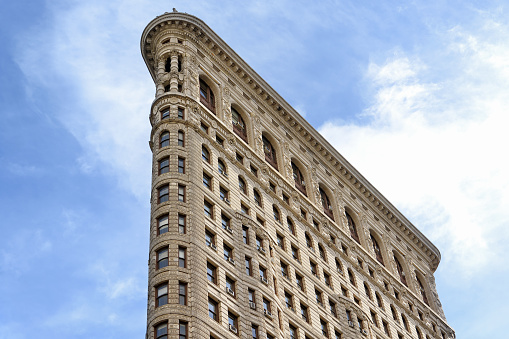 Close-up view of the famous Flatiron Building against cloudy blue sky taken from intersection of Fifth Avenue and Broadway in Manhattan, New York City, USA