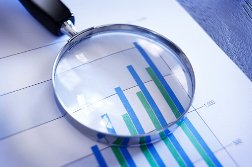 A magnifying glass rests on top of a bar graph that shows increasing sales or performance over a quarterly basis.  The image is photographed using a very shallow depth of field.