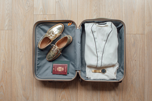 From above photo of a suitcase with passport woman's clothes shoes and watch.