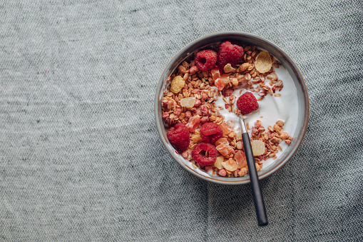 From above photo of bowl with yoghurt, cereal and raspberries for healthy meal.