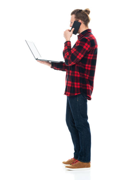istock Caucasian male standing in front of white background wearing plaid shirt and using computer 1226833440