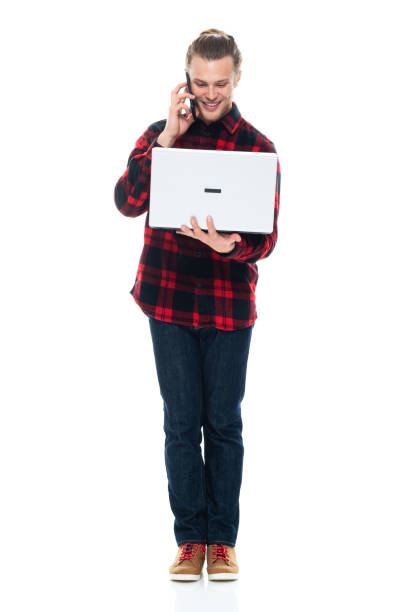 istock Caucasian male standing in front of white background wearing plaid shirt and using computer 1226833443