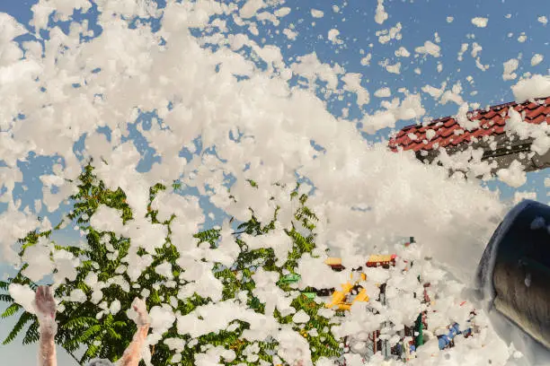 Photo of Foamy disco party. Hands raised up catch white foam. Lather maker gun blows foam into the air.