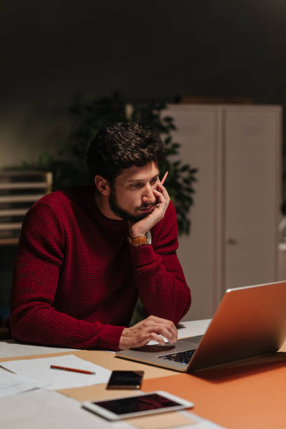 istock Handsome Young Businessman in a Red Sweater Using a Laptop Computer at the Office Late at Night 1226833684