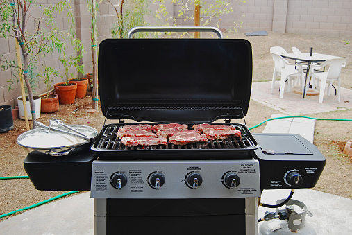 A home barbecue with steaks grilling in the backyard.