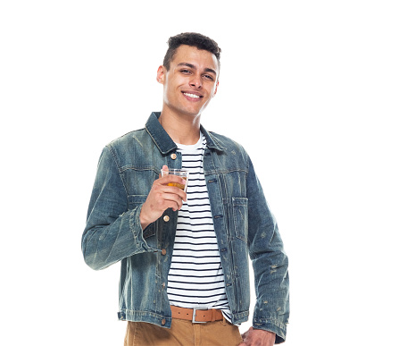 Full length of aged 20-29 years old who is tall person african-american ethnicity young male standing in front of white background wearing denim jacket who is smiling and holding drinking glass