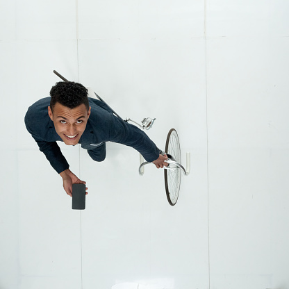 Aerial view of with curly hair african ethnicity male businessman standing in front of white background wearing smart casual who is cheerful and using bicycle