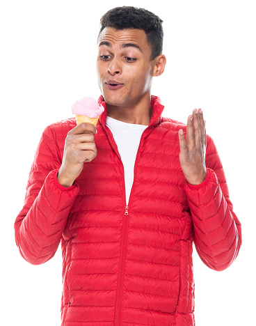 Waist up of aged 20-29 years old with black hair african ethnicity male standing in front of white background wearing pants who is laughing and holding ice cream