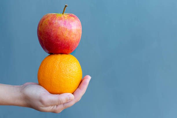 una persona sosteniendo una manzana y una fruta de naranja. dieta alimentaria saludable. - comparison apple orange isolated fotografías e imágenes de stock