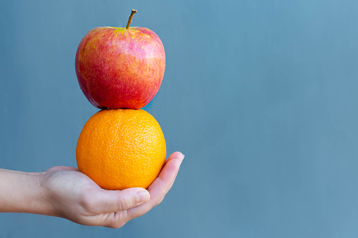 A hand holding a stack of orange and apple in front of a blue background.